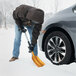 A person using a True Temper 3-in-1 folding emergency snow shovel with an aluminum blade to clear snow near a car tire.