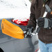 A person holding a True Temper 3-in-1 folding emergency snow shovel with an orange aluminum blade, designed for snow removal and equipped with an ice scraper and brush.