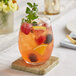 A clear stemless wine glass filled with a colorful fruit-infused beverage, garnished with fresh mint and assorted fruit pieces.