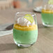 A 9 oz. stemless wine glass filled with a layered green dessert, topped with whipped cream, yellow crumbles, and a green garnish.
