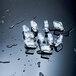 A group of small, clear ice cubes with a rectangular shape on a wet, reflective surface.