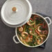 A white round casserole dish with handles and a lid, filled with shrimp and vegetable soup.