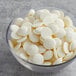 A glass bowl filled with white chocolate coating wafers.