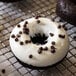 A chocolate donut topped with white icing and chocolate chips on a cooling rack.