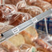A gray clip-on label holder attached to a wire basket shelf, used for organizing and labeling products such as bread.