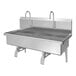 A stainless steel, wall-mounted, two-person sink with knee pedal hands-free operation and dual faucets.
