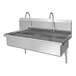 A stainless steel, wall-mounted, two-person hands-free sink with dual faucets and sensor controls.