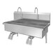 A stainless steel, wall-mounted, two-person sink with double faucets and knee pedal hands-free operation.