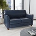 A navy blue leather loveseat with wooden feet.