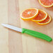A Victorinox paring knife with a green handle next to slices of oranges.