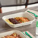 A rectangular compostable fiber food container filled with rice, black beans, vegetables, and grilled chicken.