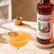 A bottle of Monin Premium Toasted Coconut Flavoring Syrup next to a cocktail glass with a dried citrus garnish.