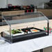 A black Carlisle single sneeze guard on a salad bar with food in a glass case.