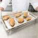 A person in white gloves holding a Vollrath stainless steel hotel pan filled with fried chicken.