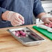 A woman using a knife to cut onions on a cutting board in a stainless steel steam table pan.