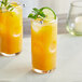 A tall glass of orange-yellow passion fruit drink with ice, garnished with a lime slice and mint sprig.
