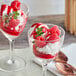 A glass dessert dish filled with vanilla ice cream, fresh raspberries, raspberry puree, and a sprig of mint.