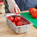 A person in gloves cutting a tomato in a Vollrath stainless steel hotel pan.