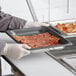 A person in a white coat holding a Vollrath stainless steel steam table pan filled with bacon.