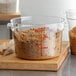 A clear round 12-quart polycarbonate food storage container filled with brown sugar, featuring red measurement markings on the side.