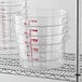 A set of clear round polycarbonate food storage containers with red measurement markings and side handles, stacked on a metal shelf.