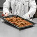 A chef holding a Vollrath stainless steel tray of food.