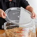 A clear round polycarbonate food storage container lid being placed on a large container filled with brown sugar.
