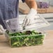 A clear polycarbonate handled lid being placed on a food storage container filled with leafy greens.