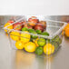 A clear polycarbonate food pan filled with lemons and limes.