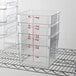 A stack of clear square polycarbonate food storage containers with red measurement markings, each with a 6-quart capacity.