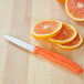 A small paring knife with a tangerine orange handle next to sliced oranges on a wooden cutting board.