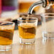 A clear 1.5 oz. shot glass being filled with a golden liquid.