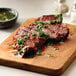 A sliced plant-based vegan steak filet topped with green herb sauce on a wooden cutting board.