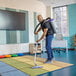 A person using a ProTeam GoFit 6 cordless backpack vacuum with a multi-surface wand kit to clean a classroom carpet.