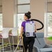 A person wearing a ProTeam GoFit 6 backpack vacuum with an attached hose and cleaning tool in an indoor setting.