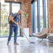A cordless backpack vacuum cleaner being used to clean a modern indoor space.