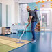 A cordless backpack vacuum being used to clean a carpeted area in an office or classroom setting.