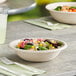 A compostable fiber take-out bowl filled with salad, placed on a table with utensils and a drink nearby.