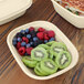 A compostable fiber box containing sliced kiwi, raspberries, blackberries, and blueberries.