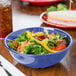 A peacock blue melamine bowl filled with salad and a sandwich on a table.