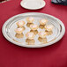A Vollrath stainless steel round serving tray with small pastries on it.