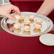 A hand holding a Vollrath stainless steel round serving tray with small cupcakes.