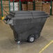 A large black Rubbermaid hinged dome lid on a black garbage bin in a warehouse.