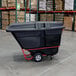 A black Rubbermaid hinged dome lid on a black tilt truck in a warehouse.