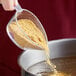 A person pouring Chicken Soup Base into a bowl of liquid.