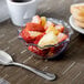 A glass bowl of fruit with a spoon in it.