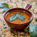 A Carlisle Lenox brown handled soup bowl filled with soup and topped with leaves.