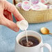 A person using a Hood Half & Half creamer to pour into a cup of coffee.