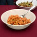 A tan SuperMel melamine bowl filled with food with a spoon in it.