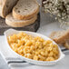 A white oval casserole dish filled with macaroni and cheese next to sliced bread.